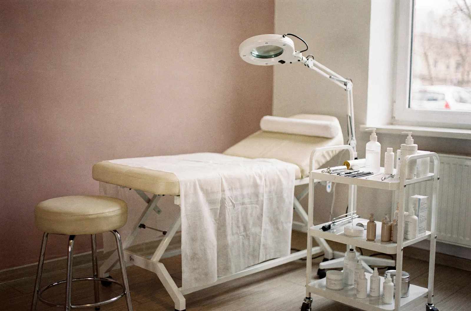 Leżanka z jednorazowym podkładem, taboret, lampa z lupą i biały wózek w gabinecie