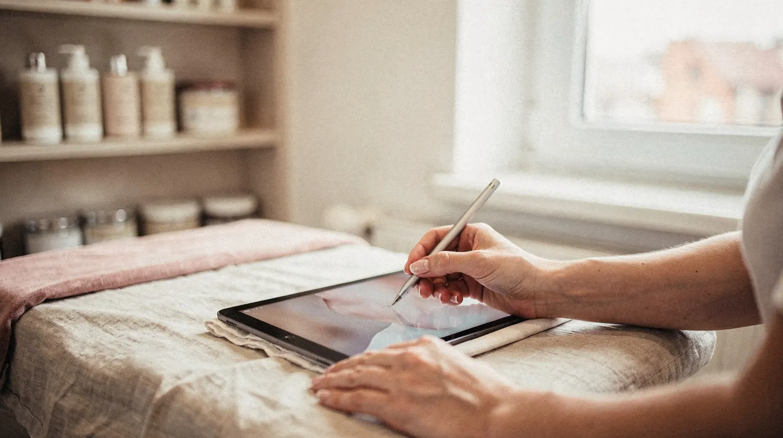 Dłoń klientki podpisuje dokument rysikiem na tablecie leżącym na leżance w gabinecie